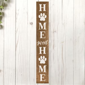 以下が含まれることがあります： 白いペンキで「Home Sweet Home」と書かれた木製の看板。文字は肉球の跡で囲まれています。