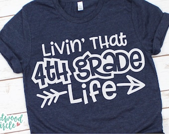May include: A navy blue t-shirt with white text that reads "Livin' That 4th Grade Life" with an arrow pointing to the right.