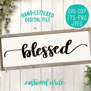 May include: A white wooden sign with the word "blessed" written in black cursive script. The sign is framed in a light brown wood frame. The text "eastwood circle" is written in teal cursive script below the word "blessed".