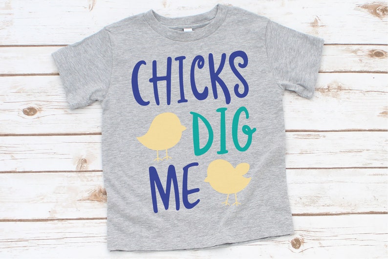 May include: A gray t-shirt with the text "CHICKS DIG ME" in blue and teal lettering. Two yellow chicks are on either side of the text.