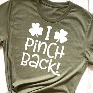 Puede incluir: Una camiseta verde con texto blanco que dice "I Pinch Back!" y dos dise&ntilde;os de tr&eacute;bol.