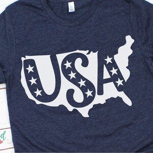 Puede incluir: Camiseta azul marino con un contorno blanco de los Estados Unidos, la palabra "USA" y estrellas. La camiseta tiene mangas enrolladas y cuello redondo. La marca "Eastwood Circle" est&aacute; impresa en la esquina inferior izquierda.