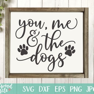 以下が含まれることがあります： 茶色の枠が付いた白い看板に、黒い筆記体で「You, Me & the Dogs」という文字が書かれています。文字の両側に黒い肉球の跡が2つあります。