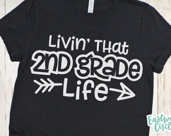 Pode incluir: Camiseta preta com texto branco que diz "Livin' That 2nd Grade Life" com uma seta branca apontando para a direita e para a esquerda.