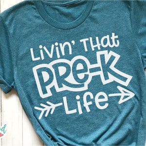 Puede incluir: Una camiseta azul turquesa con texto blanco que dice "Livin' That Pre-K Life" con una flecha apuntando hacia la derecha.
