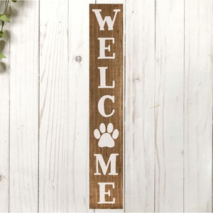 以下が含まれることがあります： 白い文字で「WELCOME」と書かれた木製のウェルカムサイン。中央に白い肉球の跡があります。サインは白い木製の背景に置かれています。