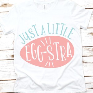 May include: White t-shirt with a pink oval and the text "Just a little egg-stra" in blue.
