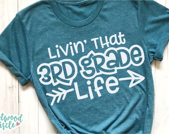 Pode incluir: Camiseta azul turquesa com texto branco que diz "Livin' That 3rd Grade Life" com uma seta branca apontando para a direita.