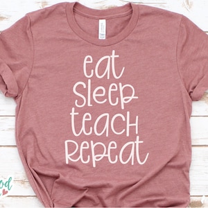 Puede incluir: Una camiseta de color malva con el texto "eat sleep teach repeat" en blanco.