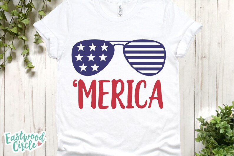 Puede incluir: Camiseta blanca con un dise&ntilde;o patri&oacute;tico. El gr&aacute;fico presenta gafas de sol con rayas y estrellas azules y blancas, y la palabra "'MERICA" en rojo. Un dise&ntilde;o divertido y festivo para el D&iacute;a de la Independencia.