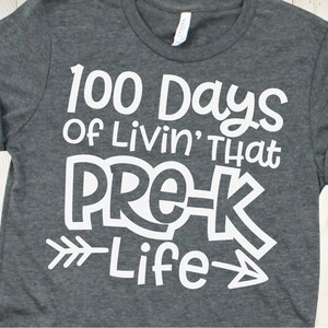Puede incluir: Una camiseta gris con texto blanco que dice "100 Days of Livin' That Pre-K Life" con una flecha apuntando hacia la derecha.