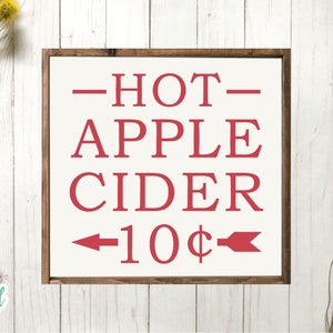 May include: A framed wooden sign with the words "HOT APPLE CIDER" in red, with an arrow pointing left and the text "10&cent;". The sign is on a white background with a wooden frame.