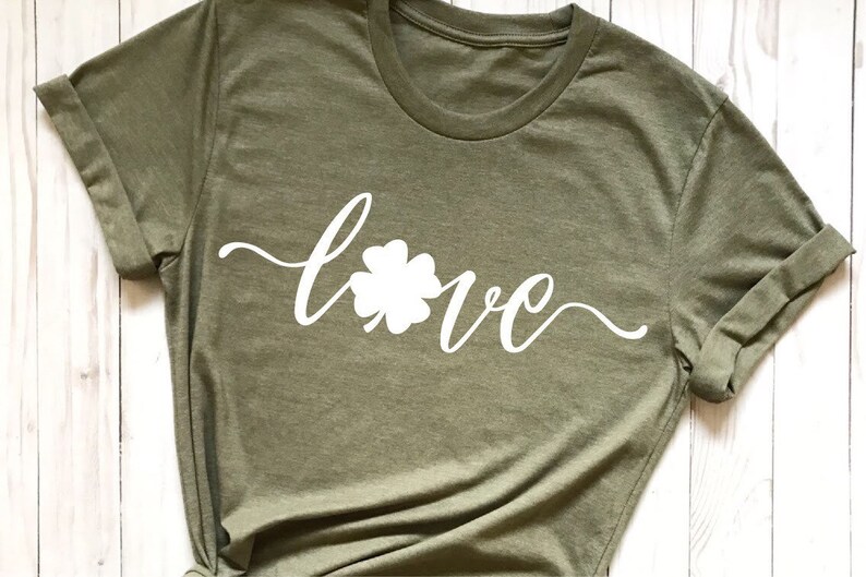 Puede incluir: Una camiseta verde con un tr&eacute;bol de cuatro hojas blanco y la palabra "love" escrita en cursiva.