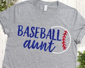 May include: Gray t-shirt with blue glitter text that says "Baseball aunt" and a white baseball with red stitching.