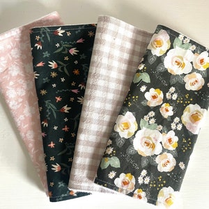 May include: Set of four fabric squares with different patterns. One square is pink with a floral pattern, one is black with a floral pattern, one is black with a small floral pattern, and one is white and gray with a gingham pattern.
