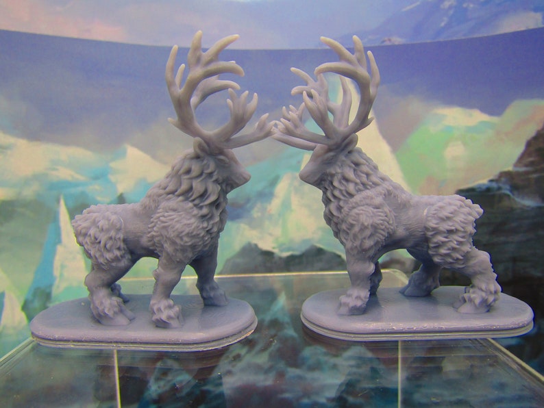 May include: Two gray, furry, miniature figurines of deer with large antlers. The deer are facing each other and are standing on small, gray bases.