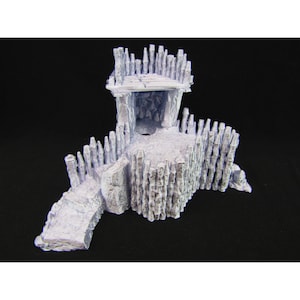 May include: A gray, 3D printed miniature of a small, fortified structure with a wooden palisade and a small, open doorway. The structure is built on a raised platform with a ramp leading up to the entrance.