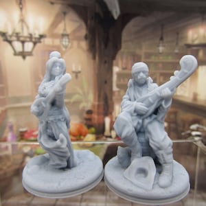 May include: Two gray painted figurines of musicians playing instruments. The female figurine is holding a lute and the male figurine is holding a lute with a scroll design. Both figurines are standing on round bases.