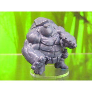 May include: A gray, detailed miniature figurine of a turtle with a muscular build, wearing a shell and a belt. The figurine is standing on a clear plastic base.