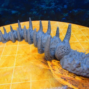 May include: A gray, 3D printed model of a long, segmented creature with a spiky, textured head. The creature has a series of pointed, jagged protrusions along its back.