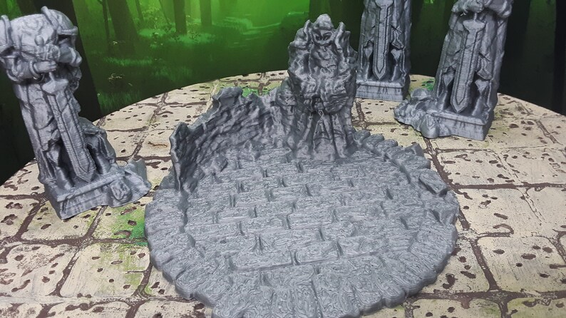 May include: A set of four gray 3D printed miniature statues of warriors holding swords, standing on a gray circular base with a textured surface. The statues are arranged around the base, with one statue in the center.