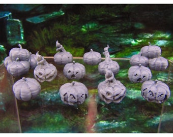 May include: A collection of 13 gray painted ceramic pumpkin figurines with various facial expressions. The pumpkins are arranged on a glass surface with a green background.