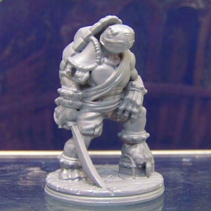 May include: A gray plastic miniature figurine of a turtle warrior holding a sword. The turtle is wearing armor and a sash. The figurine is standing on a round base.