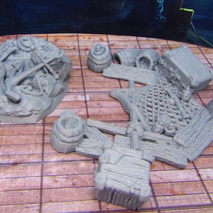 May include: A set of grey resin miniature pirate treasure props, including a chest, barrels, and an anchor. The props are designed for tabletop games and role-playing.