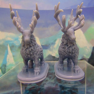May include: Two gray, furry, miniature figurines of deer with large antlers. The deer are standing on small, gray bases.