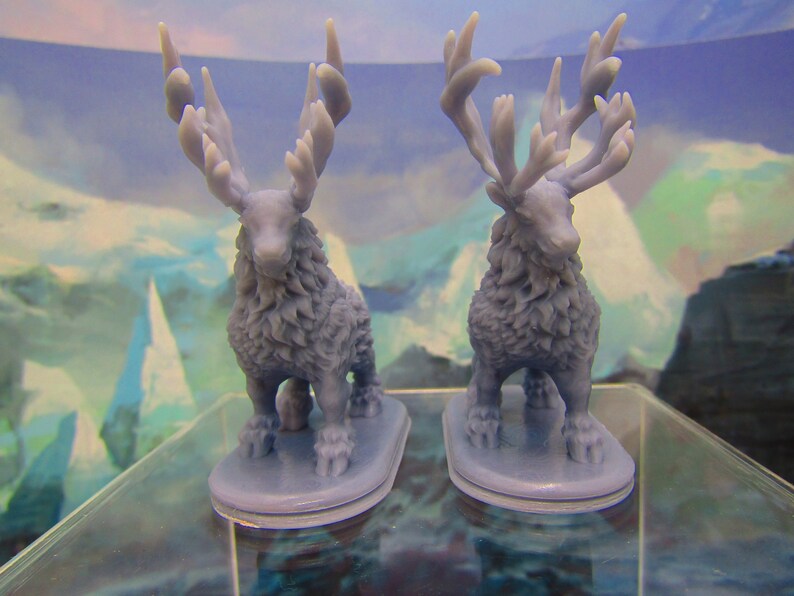 May include: Two gray, furry, miniature figurines of deer with large antlers. The deer are standing on small, gray bases.