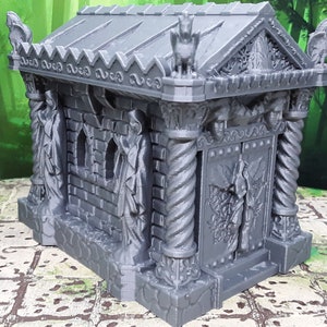 May include: A grey, 3D printed miniature of a stone mausoleum with a detailed design. The mausoleum has a door with a sculpted design, two columns, and two figures on the sides. The roof has a decorative design and a gargoyle on top.