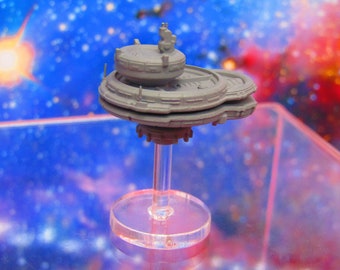 May include: A gray, multi-level space station model with a clear plastic stand. The model is set against a blurred background of a galaxy with stars and nebulae.