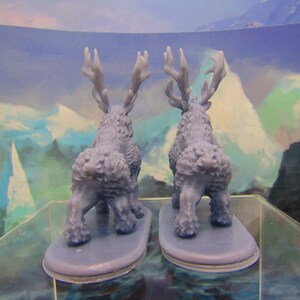 May include: Two blue plastic miniature figurines of deer with antlers, standing on a clear surface. The deer are facing away from each other.