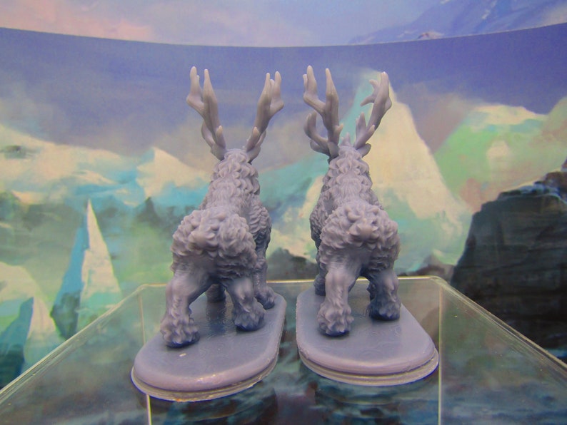 May include: Two blue plastic miniature figurines of deer with antlers, standing on a clear surface. The deer are facing away from each other.