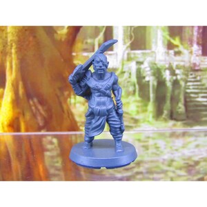 May include: A blue plastic miniature figurine of a fantasy character holding a sword. The character is wearing a loincloth and has a fierce expression.