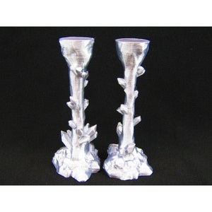May include: Two silver candle holders with a crystal-like design. The holders are tall and slender with a wide base.