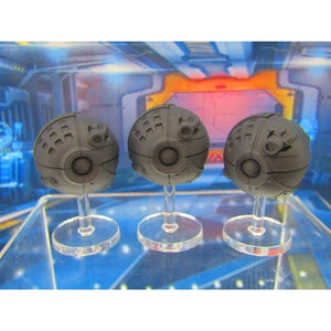 May include: Three gray, spherical, sci-fi themed miniatures with detailed surface textures and raised circular features. Each miniature is mounted on a clear plastic stand.