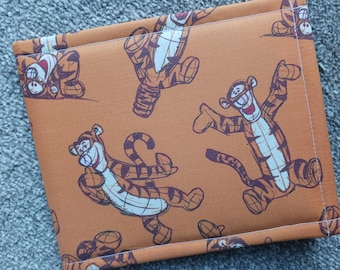 May include: Orange fabric item featuring a repeating pattern of the Tigger character from Winnie the Pooh. The design shows Tigger in various poses with brown stripes and a white belly. The item has white stitching around the edges.