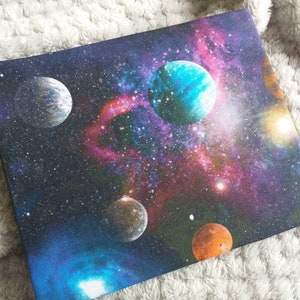 May include: A dark blue canvas with a colorful galaxy print featuring multiple planets, stars, and nebulae. The planets are various shades of blue, green, and orange.