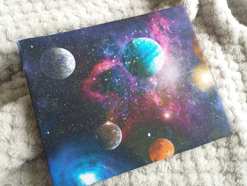 May include: A dark blue canvas with a colorful galaxy print featuring multiple planets, stars, and nebulae. The planets are various shades of blue, green, and orange.