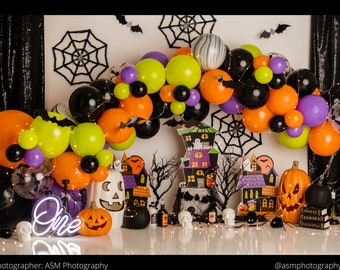 May include: A Halloween-themed balloon arch in orange, lime green, black, and purple, featuring spider web cutouts, a neon sign reading One, a jack-o'-lantern, a white ghost-faced pumpkin, and three stacked books labeled Magic Curses and Books of Spells.