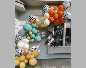 May include: A balloon arch with black and white checkered balloons, orange, yellow, and teal balloons. The arch is decorated with black balloons that spell out "TWO FAST".