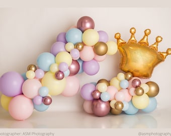 Op de afbeelding: Een gouden kroonballon met pastelkleurige ballonnen in een guirlande vorm. De ballonnen zijn in tinten roze, paars, geel en blauw.