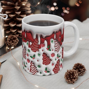 May include: White ceramic mug with a red and white Christmas tree pattern. The mug is filled with coffee and has a white handle.