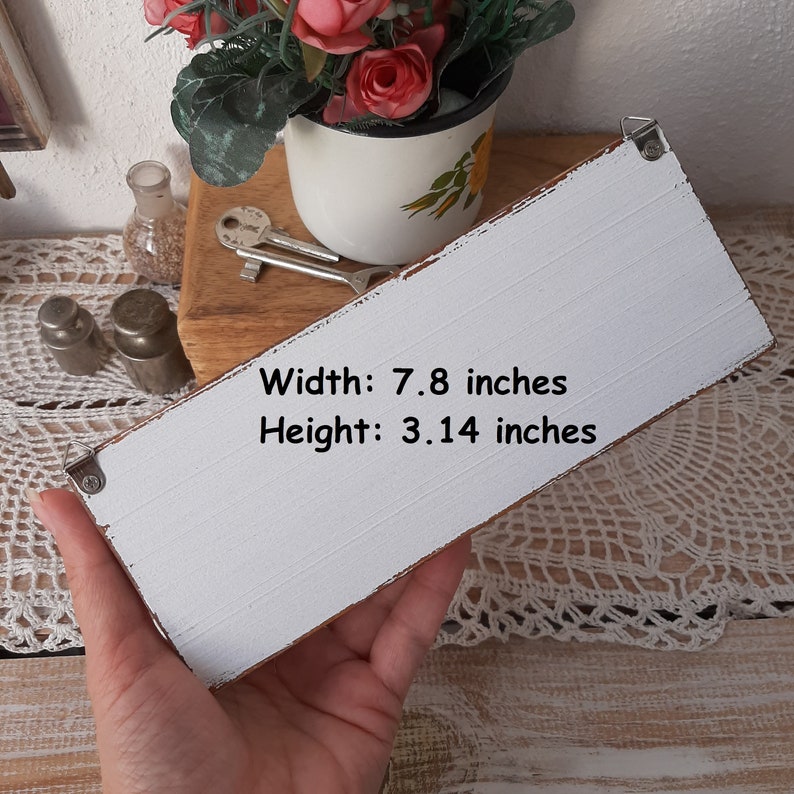 K&ouml;nnte beinhalten: Ein wei&szlig;es Holzschild mit abgenutzter Farbe und schwarzem Text, der "Breite: 7,8 Zoll H&ouml;he: 3,14 Zoll" lautet.