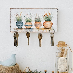 Könnte beinhalten: Schlüsselhalter aus Holz mit einem bemalten Design aus vier Topfpflanzen mit Blumen. Der Schlüsselhalter hat fünf Haken zum Aufhängen von Schlüsseln.