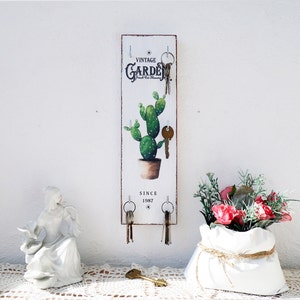 Könnte beinhalten: Weißer Holz-Schlüsselhalter mit einer Kaktus-Illustration und dem Text "Vintage Garden Fresh Cut Flowers Since 1987". Es gibt fünf Haken zum Aufhängen von Schlüsseln.