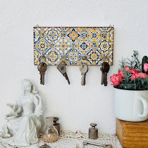 Könnte beinhalten: Ein Schlüsselhalter mit einem bunten Fliesenmuster. Der Halter hat fünf Haken und ist an einer weißen Wand montiert. An den Haken hängen fünf Schlüssel.
