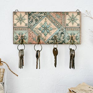 Może przedstawiać: Dekoracyjny wieszak na klucze z wzorem płytek w odcieniach niebieskiego, zielonego i beżowego. Wieszak ma pięć haczyków do zawieszania kluczy.
