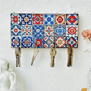May include: A key holder with a colorful tile design. The tile design features blue, red, and white colors. The key holder has five hooks for hanging keys.